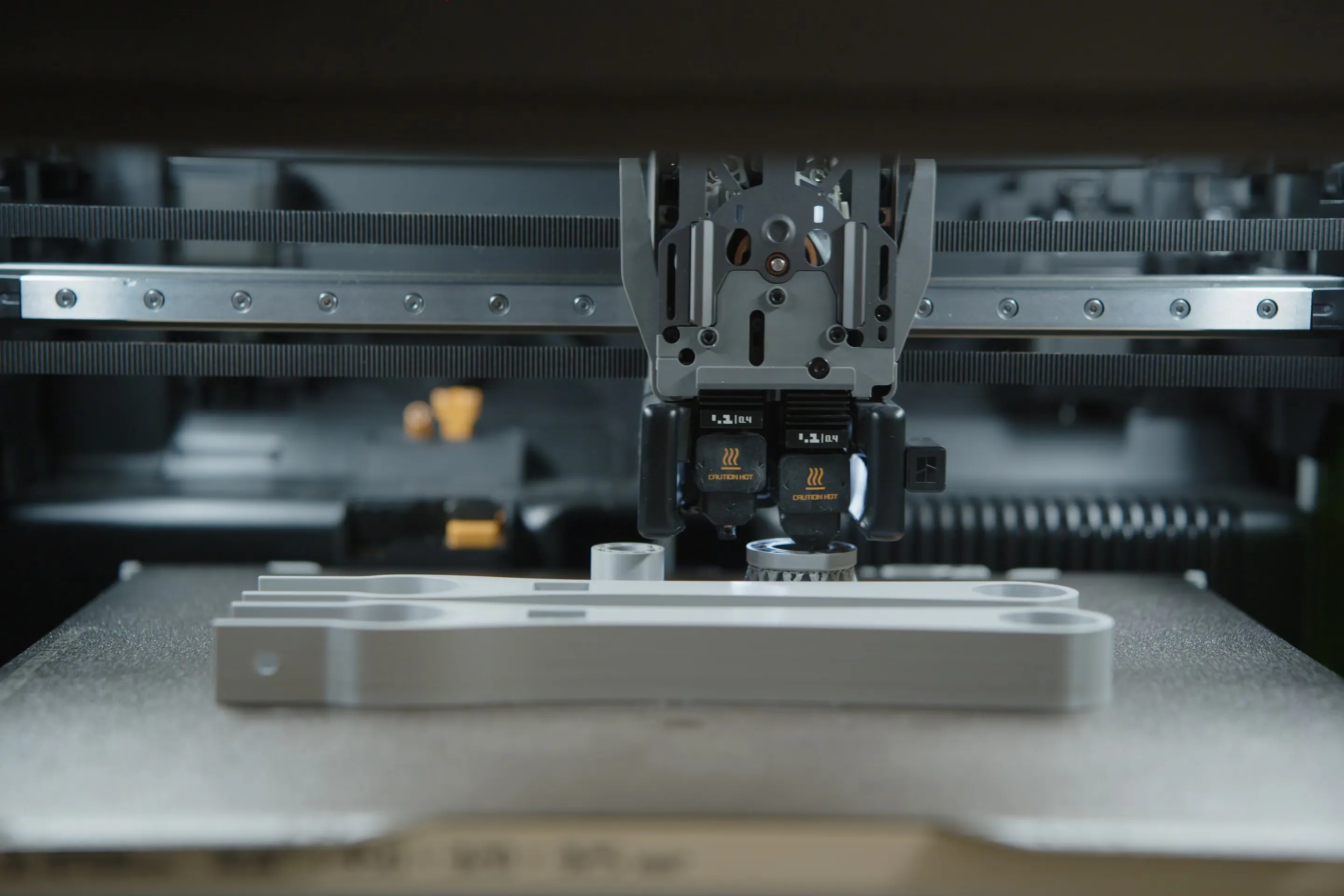 Ein 3D-Drucker druckt ein langes graues Bauteil.