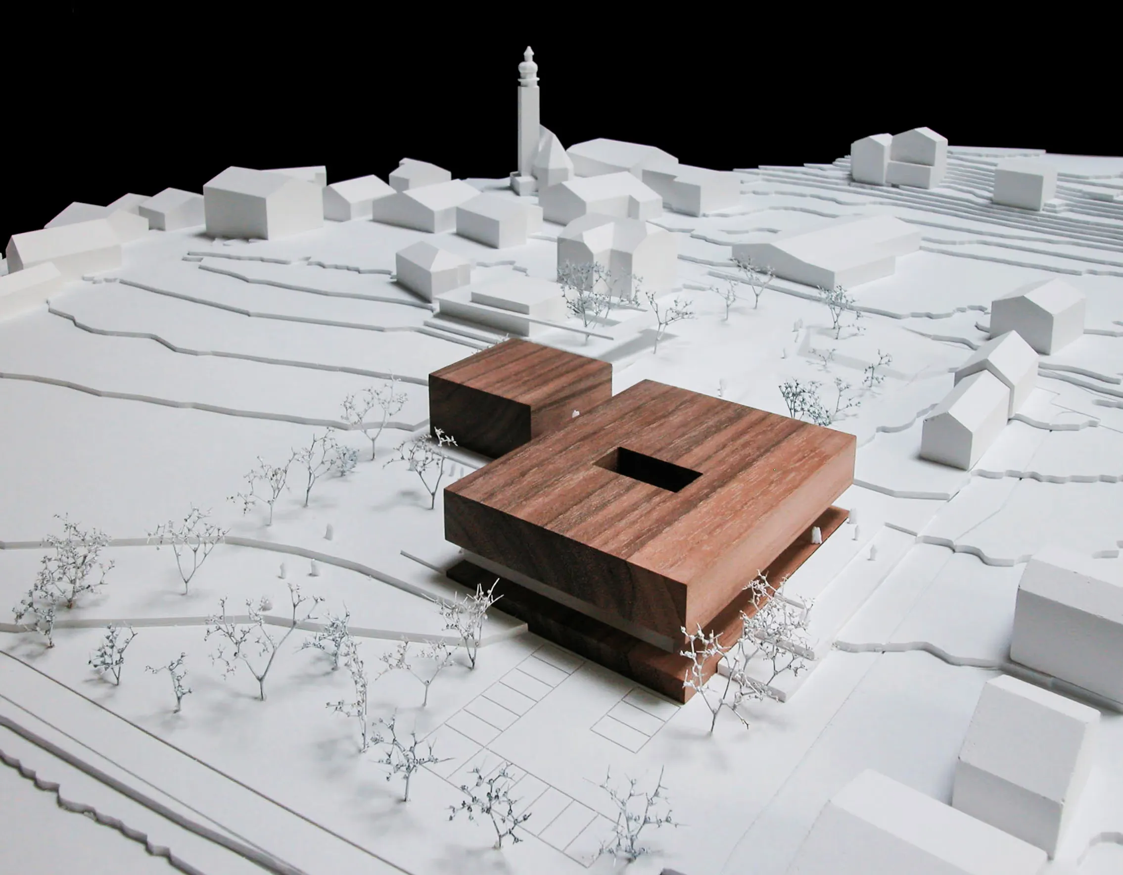 Ortsmodell mit weißen Bestandsbauten, Kirchturm und einem dunklen Holzbaukörper als Neubau.
