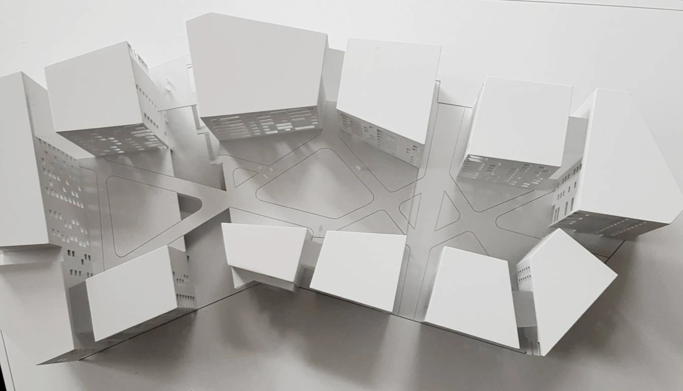 Weißes Architekturmodell aus gefalteten Flächen mit eingeschnittenen Öffnungen, von oben gesehen.